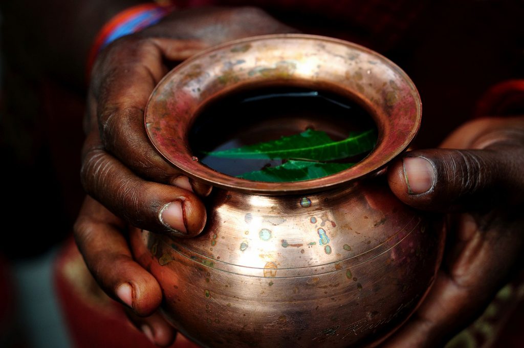 A lady is holding a metal pot with neem-leaves and water. This is considered as the part of the offerings to the Goddess.
