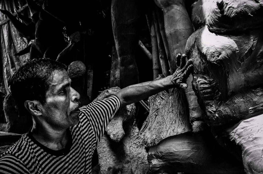 An artisan is seen as he applies a layer of mud on the idols