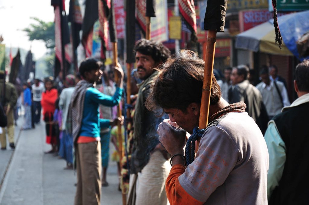 A flag-bearer lighting up his bidi during a short break as the procession moves forward.
