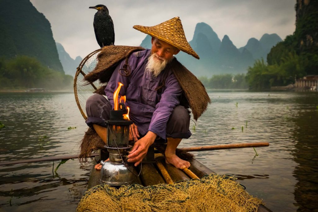 Cormorant fishing is a traditional fishing method in which fishermen use trained cormorants to fish in rivers. An aged fisherman along with his pet birds is seen as he prepares to light up his boat near the shore of Li river.