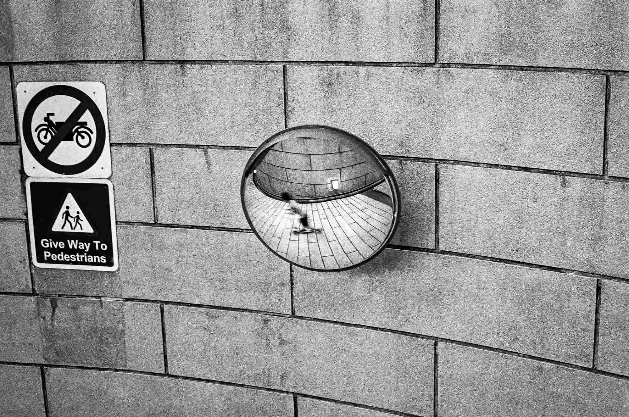 The reflection of a kid is seen as he rides his scooter.