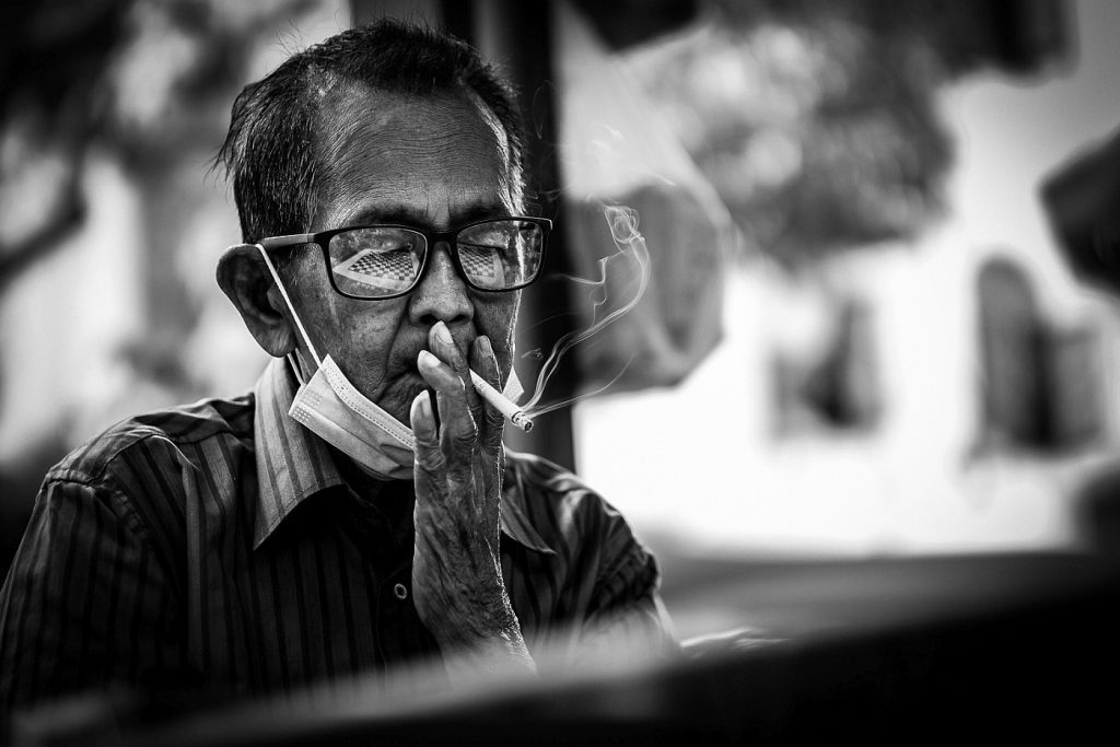 An elderly person is seen as he's engrossed in a board game while smoking. Chinatown, Singapore